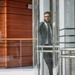 Full length portrait of confident middle-aged entrepreneur wearing classical suit conducting telephone negotiations with business partner while going up in elevator